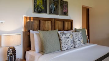 A neatly made bed with patterned pillows, a wooden headboard, and a wall-mounted artwork of scooters.