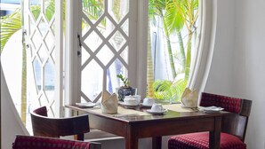 A dining area with a table set for two, surrounded by chairs with red cushions, and a large arched window with a lattice design. - Deco On 44 (Galle)
