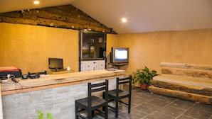 Una cocina rústica con mostrador de madera, dos taburetes de bar, un televisor y piso de baldosas de piedra.