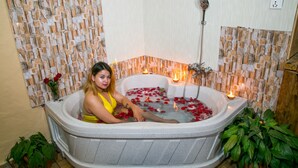 Una mujer en una bañera llena de pétalos de rosa y velas, rodeada de plantas en macetas.