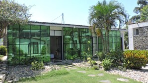A modern house with large glass windows, a stone exterior, and a well-maintained garden with palm trees and rocks. - Gantavya Resort (Pokhara)
