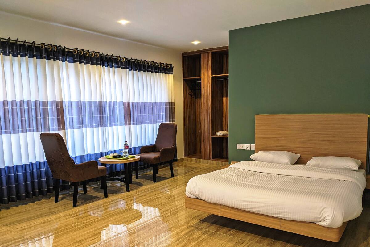 Een hotelkamer met een houten bed, een ronde tafel met stoelen en een groot raam met gordijnen.