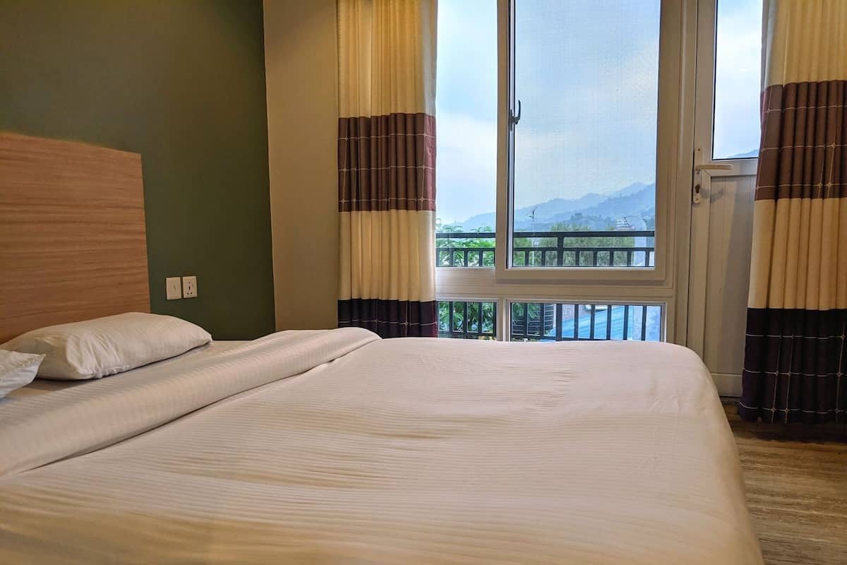 Hotelkamer met een groot bed, een houten hoofdeinde, een balkon met uitzicht op bergen en gordijnen met een patroon.
