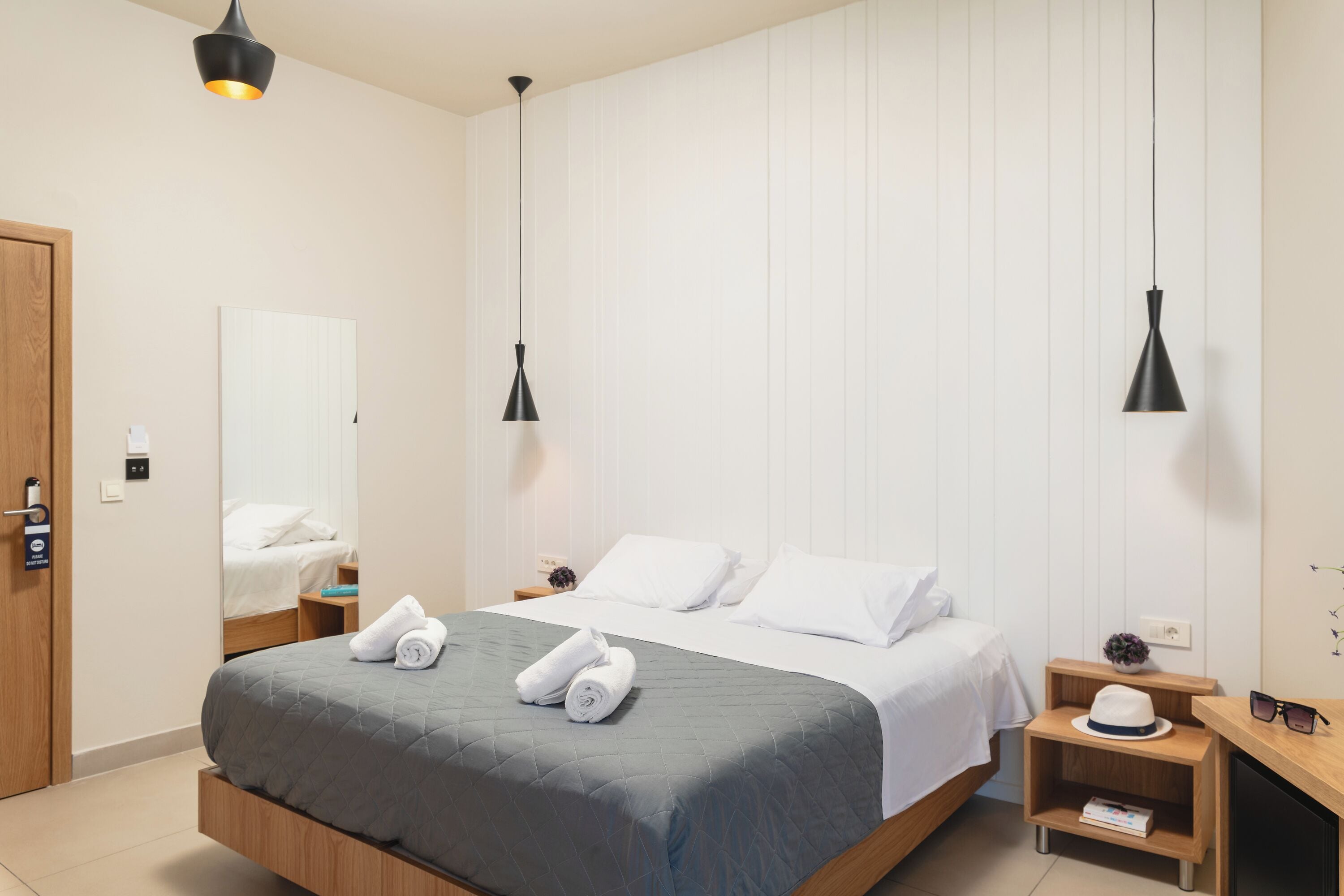 Una habitación de hotel moderna con una cama grande, dos mesitas de noche y un tocador de madera.