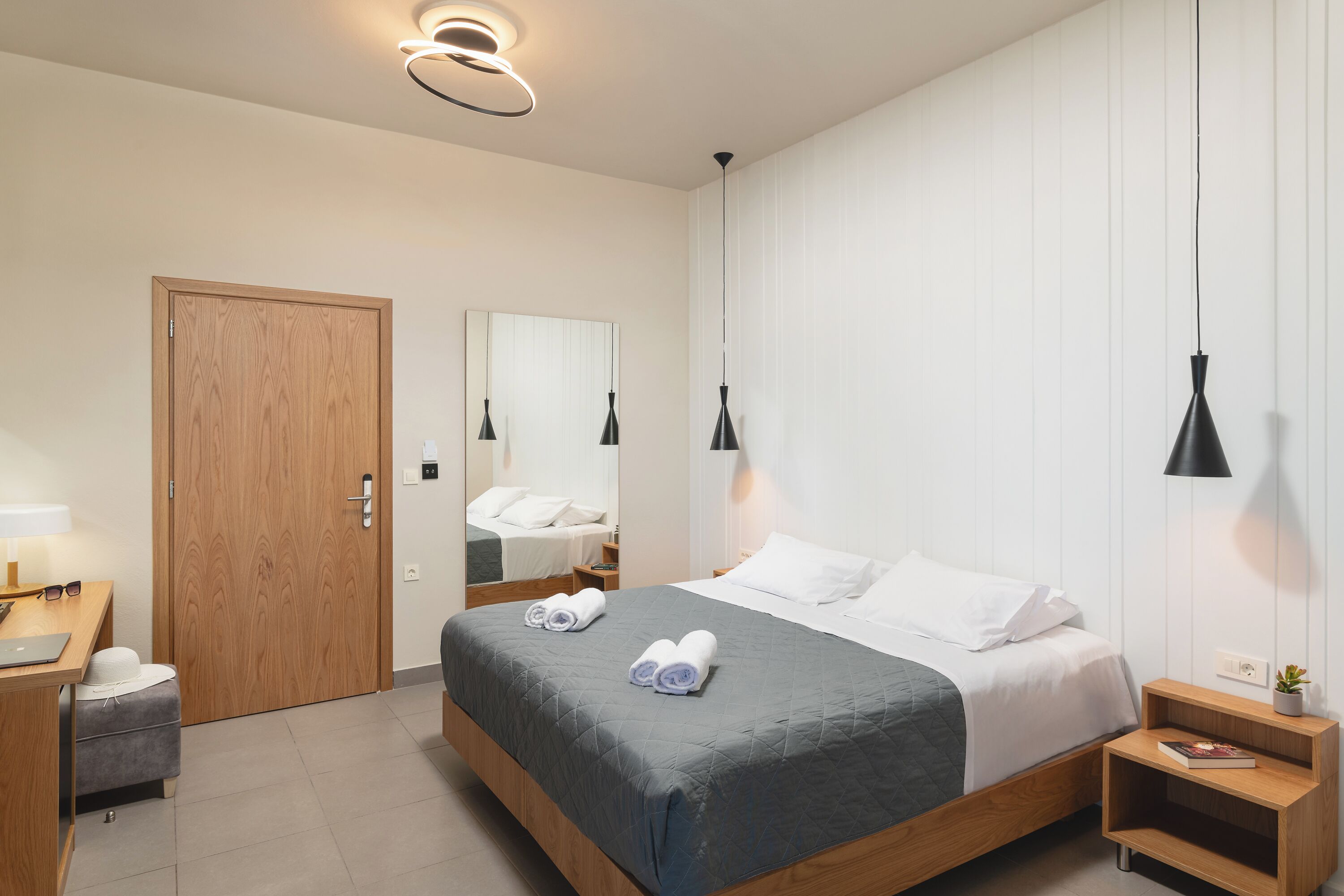 Una habitación de hotel moderna con una cama de madera, un escritorio, una silla, una mesita y un espejo.