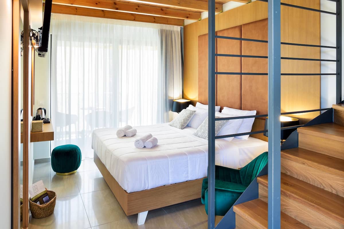 Una habitación de hotel moderna con techo de madera, una cama con sábanas blancas, un otoman verde y una escalera con escalones de madera.