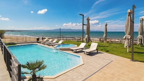 A swimming pool with lounge chairs and umbrellas, a view of the sea, and a grassy area. - Elia Agia Marina Hotel (Chania)