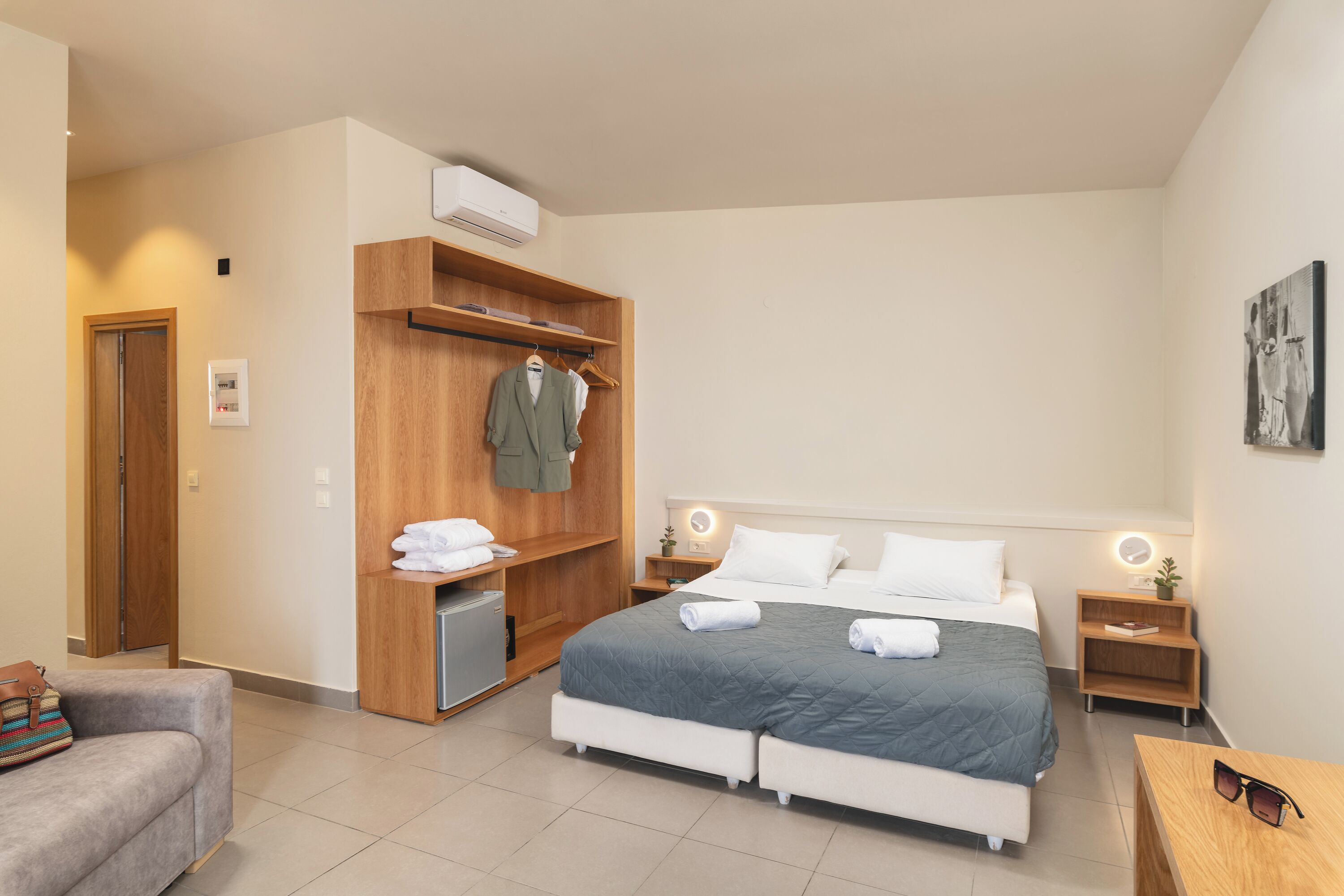 A modern hotel room with a bed, a wooden wardrobe, a small desk, and a couch.