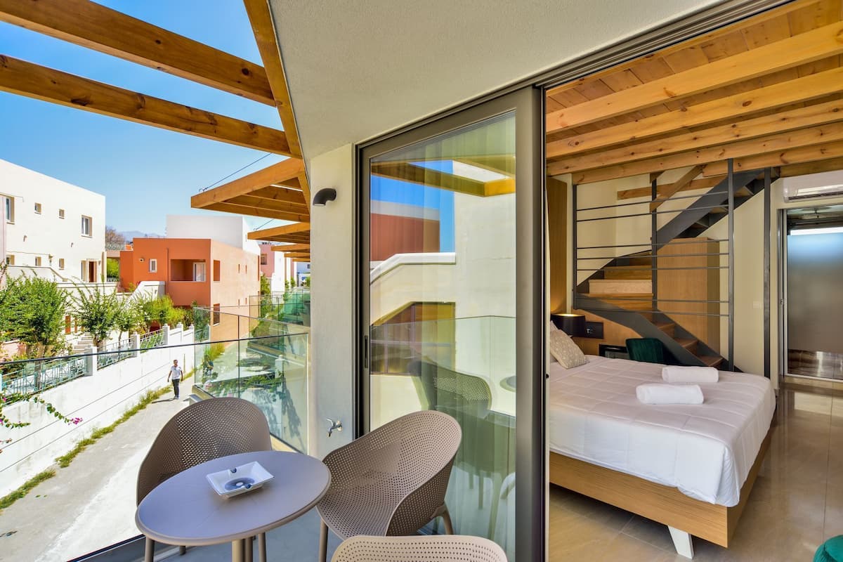 Un balcón con puerta de cristal que da a un dormitorio con cama, una silla y una mesa.