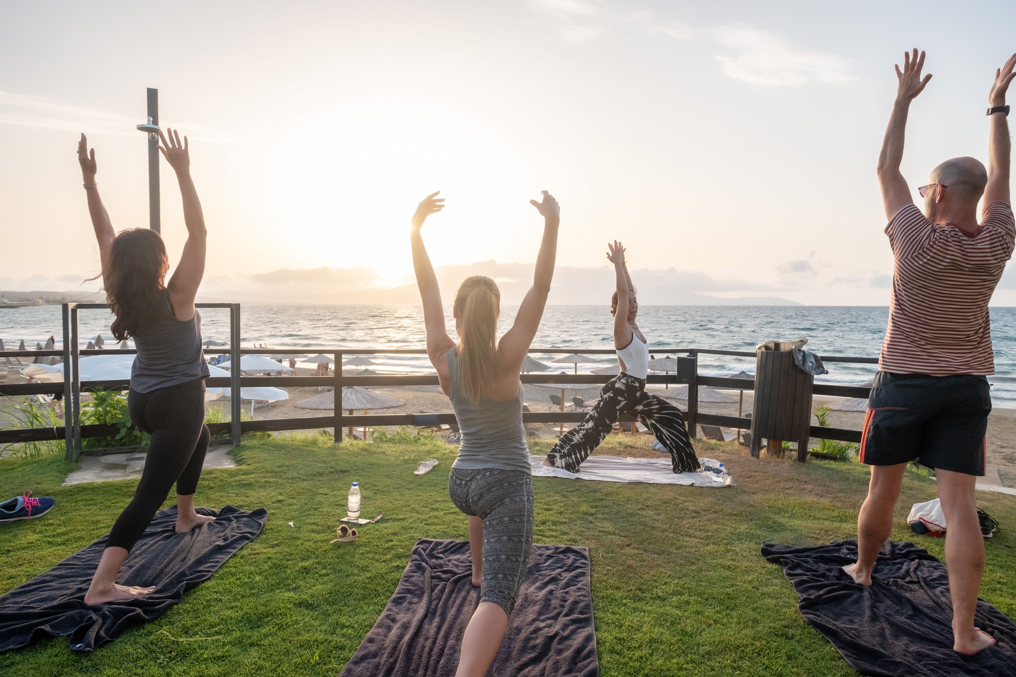 Three people performing yoga on mats by a waterfront.