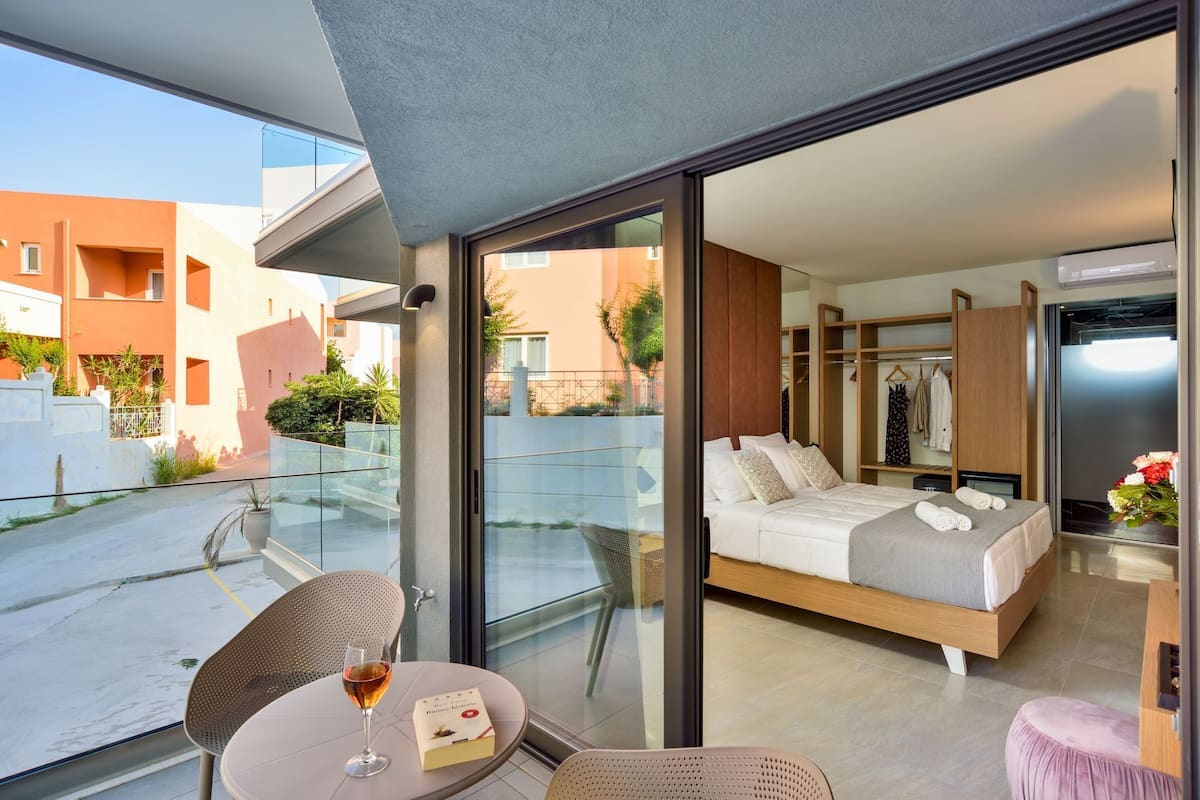 Habitación de hotel moderna con balcón, una cama, un área de descanso con una mesa de vidrio y vistas a los edificios exteriores.