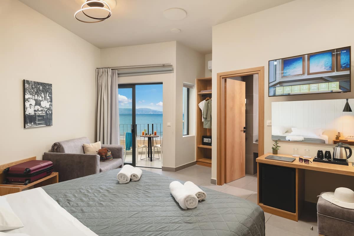 Habitación de hotel con cama, escritorio, silla, armario y vista al mar.