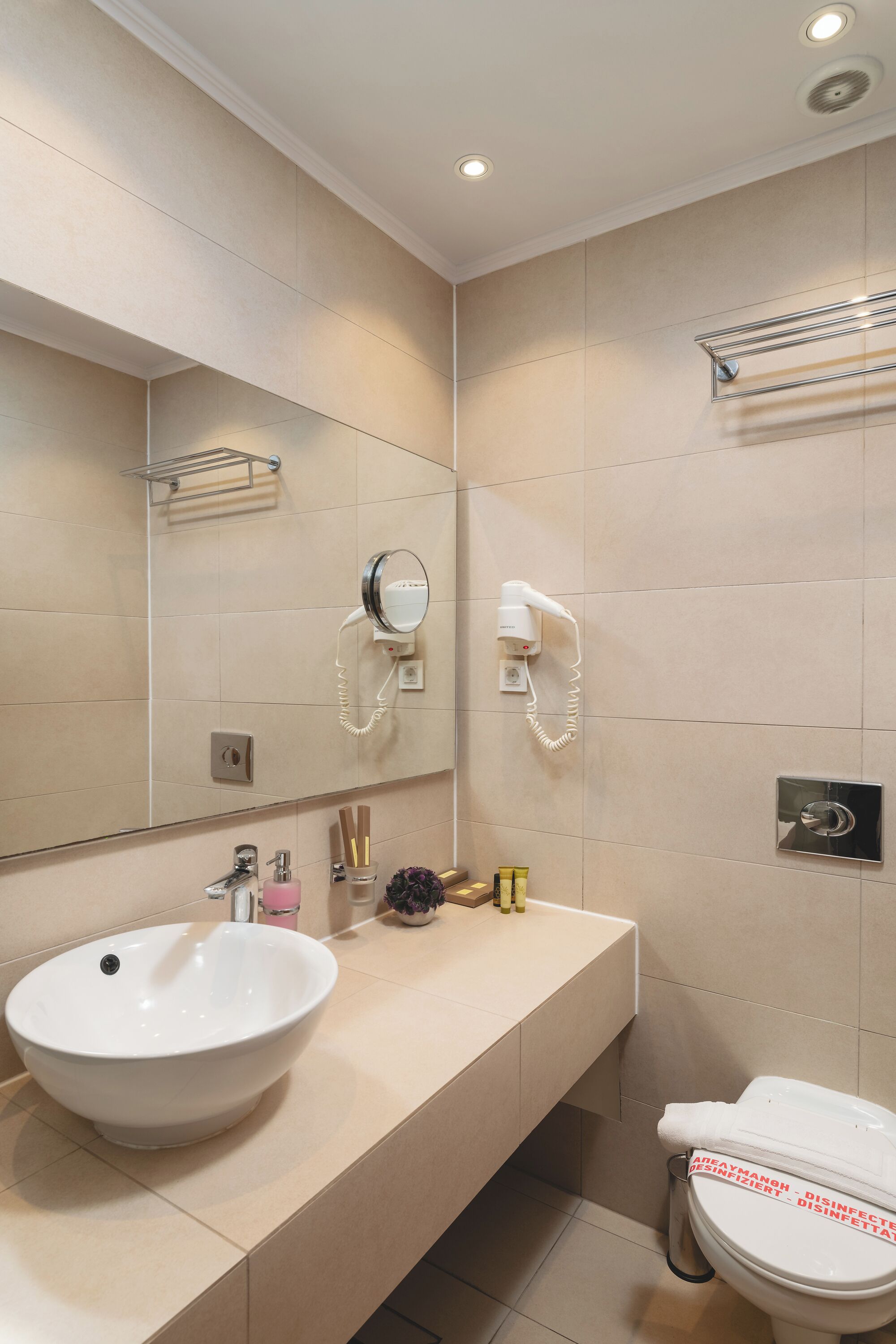 A modern bathroom with a large mirror, a sink, a toilet, and a hairdryer mounted on the wall.