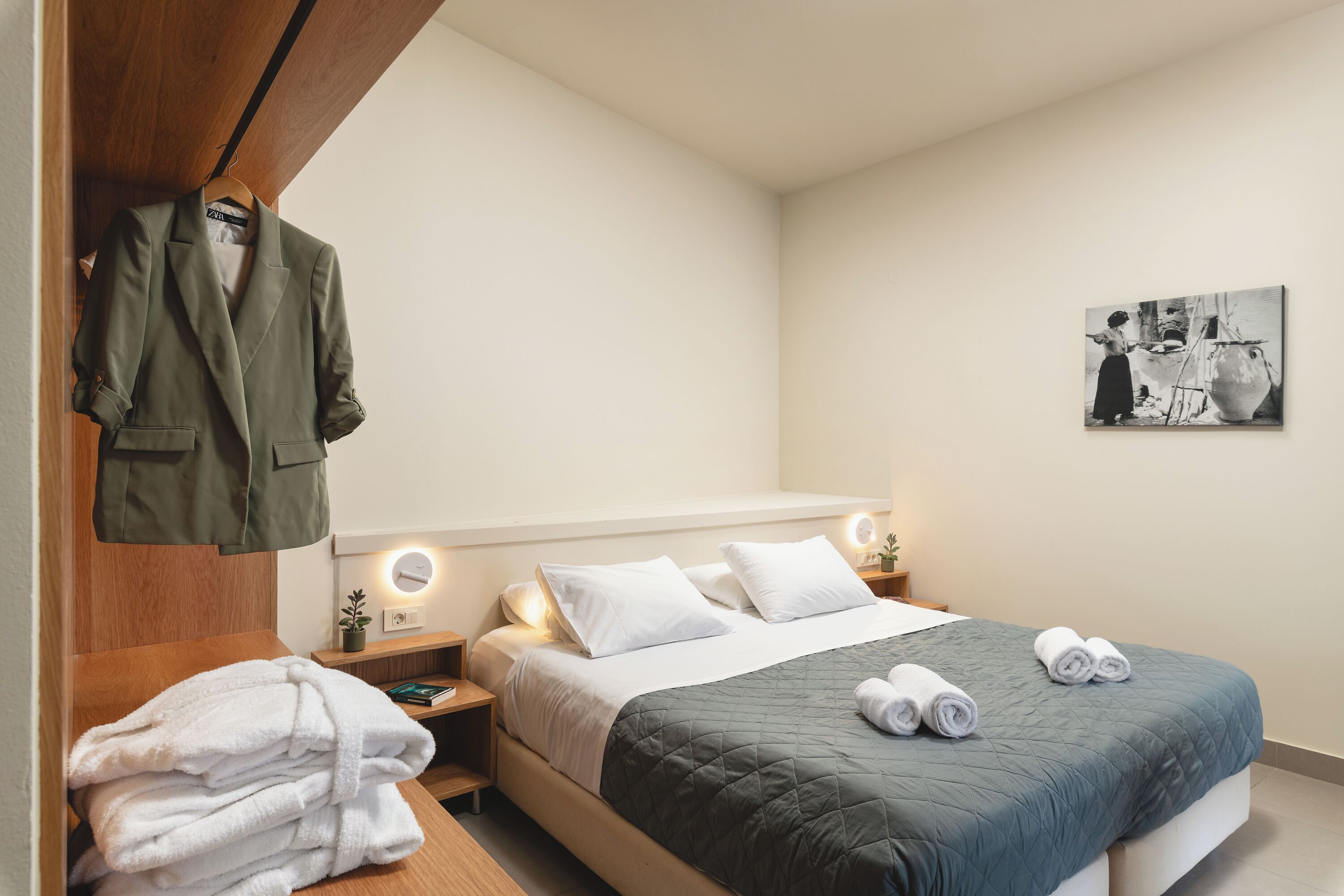 A neatly made bed with a quilted blue cover, white pillows, and rolled towels on the side.
