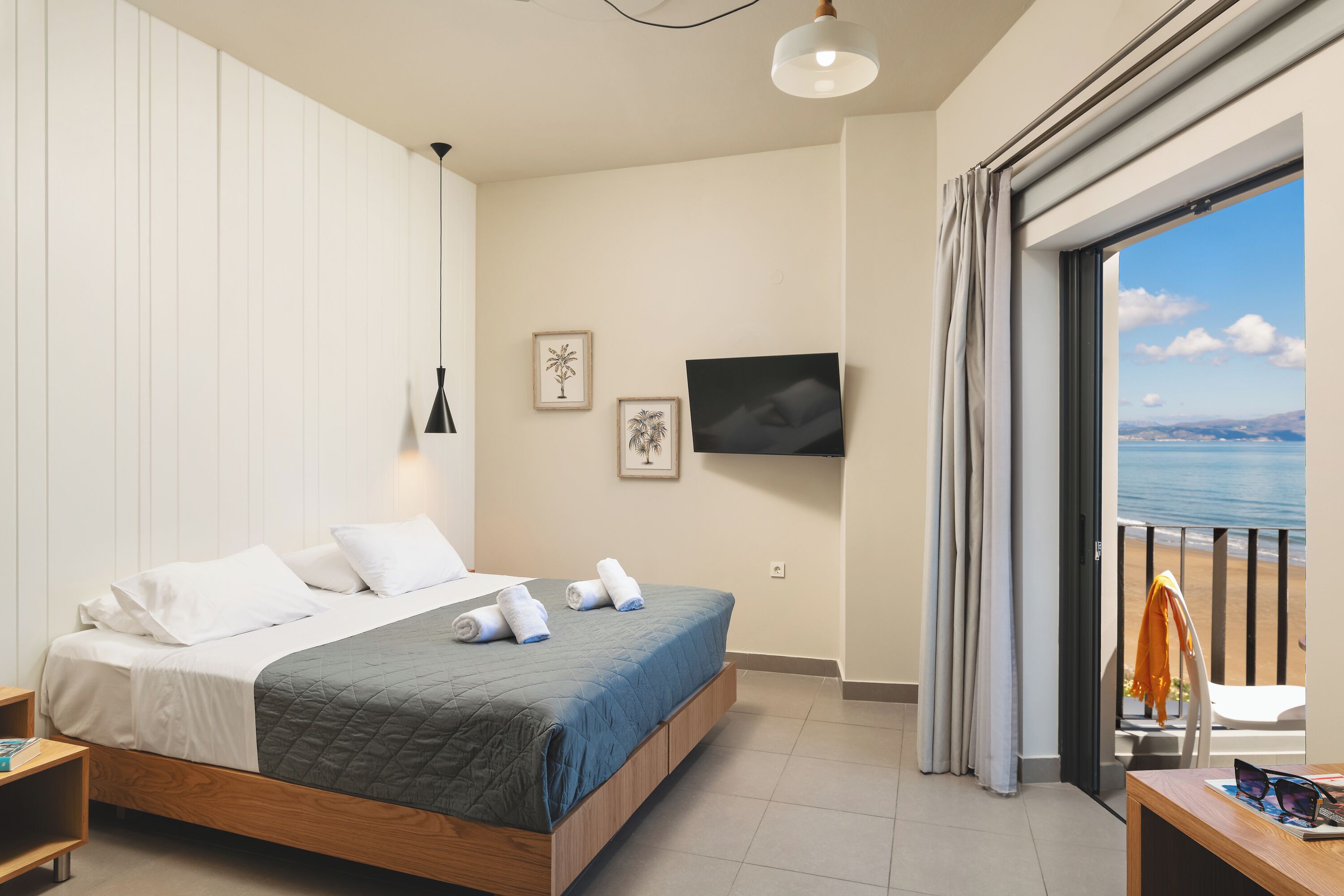 Quarto com cama, televisão, janela com cortinas e vista para o mar.