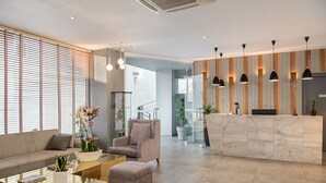A modern lobby with a sofa, armchair, and ottoman, a reception desk, and a staircase in the background. - Elia Agia Marina Hotel (Chania)