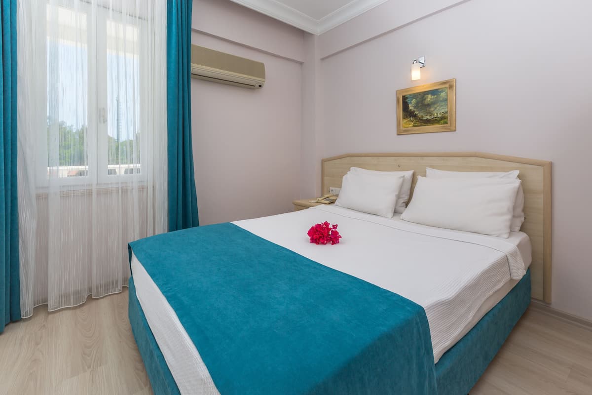 Quarto de hotel com cama, mesa de cabeceira, um quadro na parede e uma janela com cortinas.