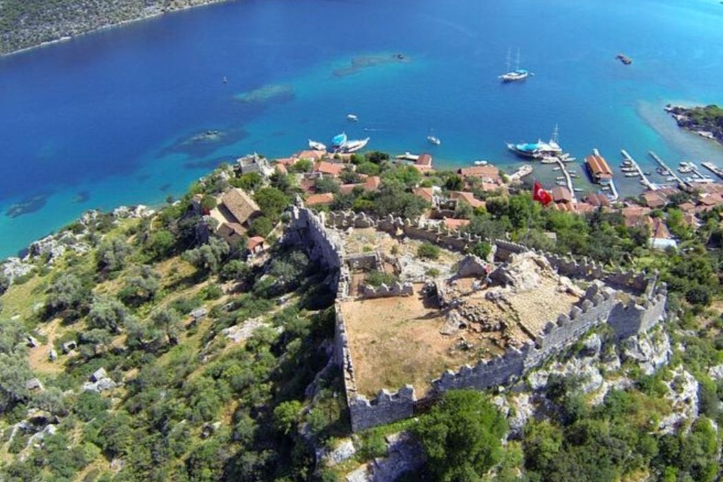An aerial view of a coastal town with a historic fortification, clear blue waters, and boats.