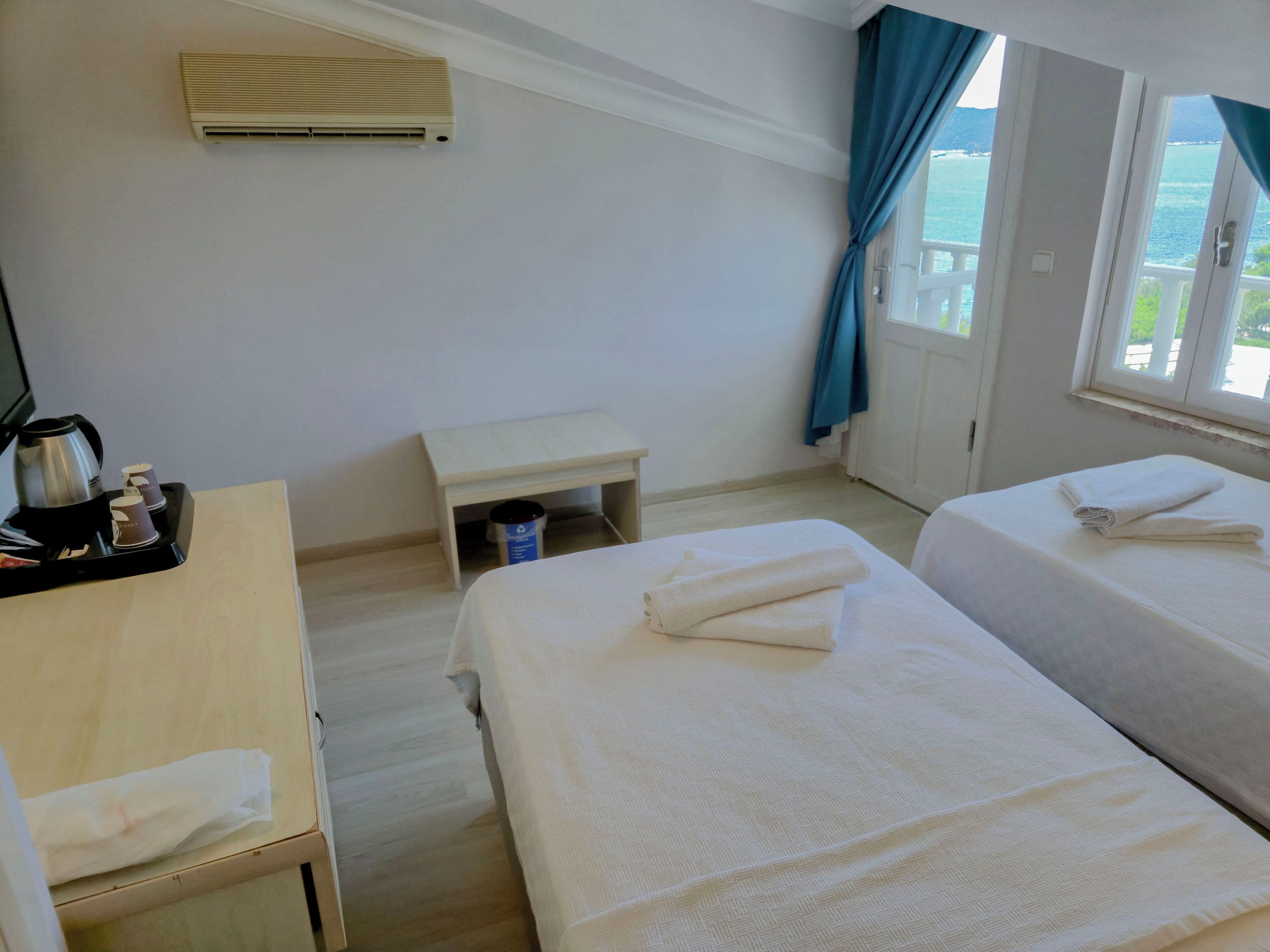 Quarto de hotel com duas camas, uma escrivaninha, máquina de café e vista para o mar.
