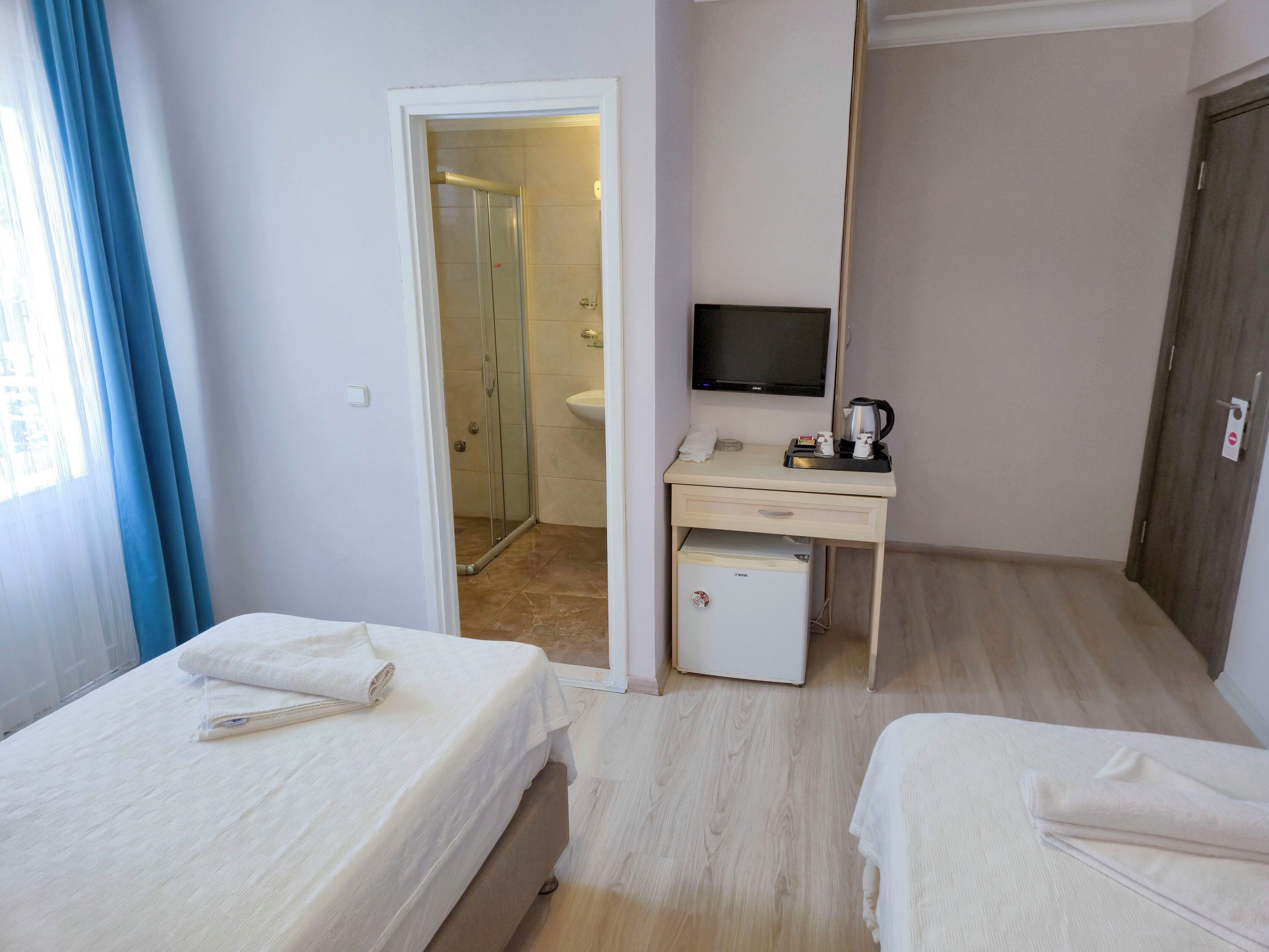 Habitación de hotel con dos camas, un escritorio, televisión, un refrigerador pequeño y zona de ducha.