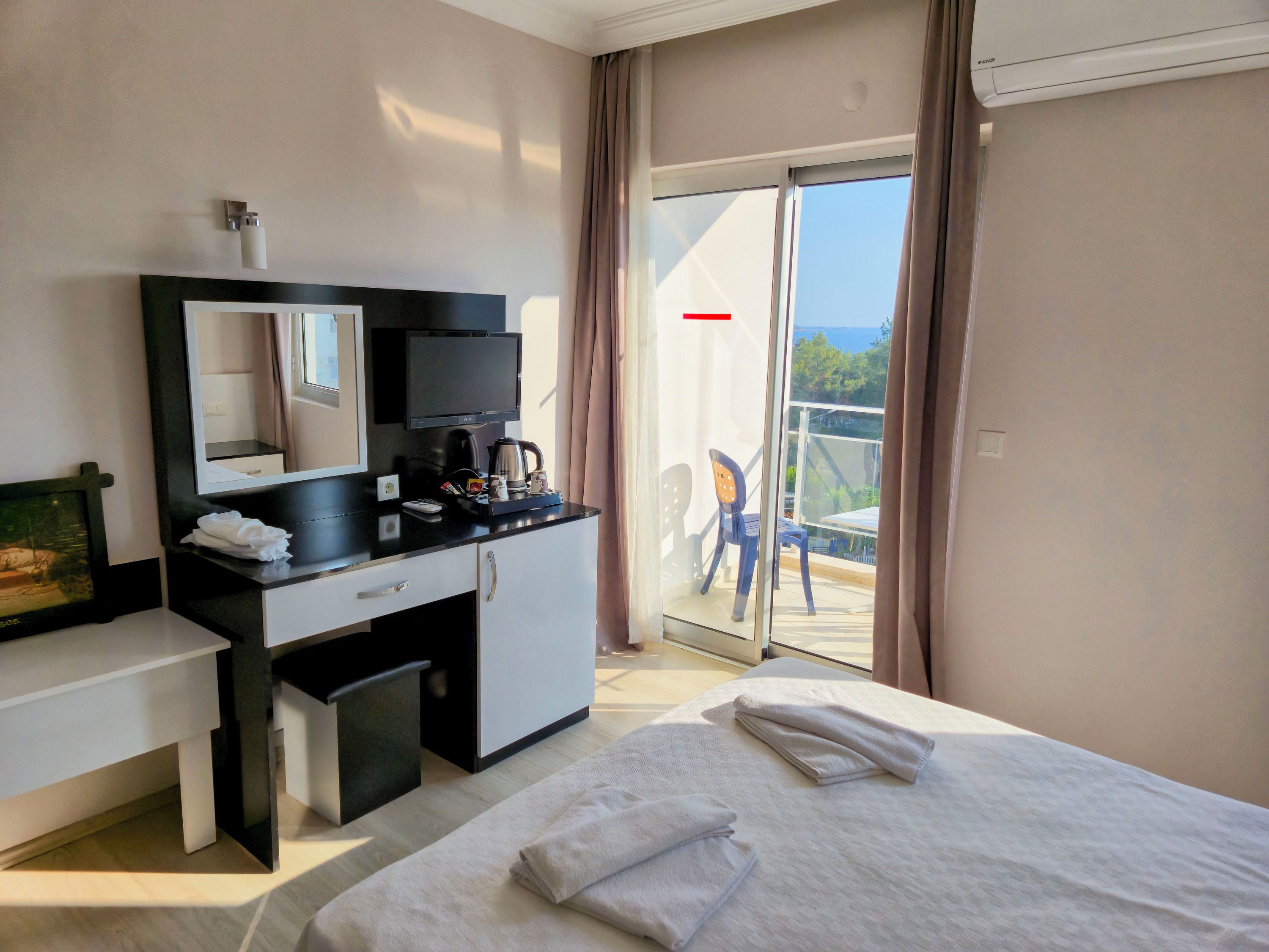 Quarto de hotel com cama, escrivaninha com espelho, cafeteira e vista para o exterior.