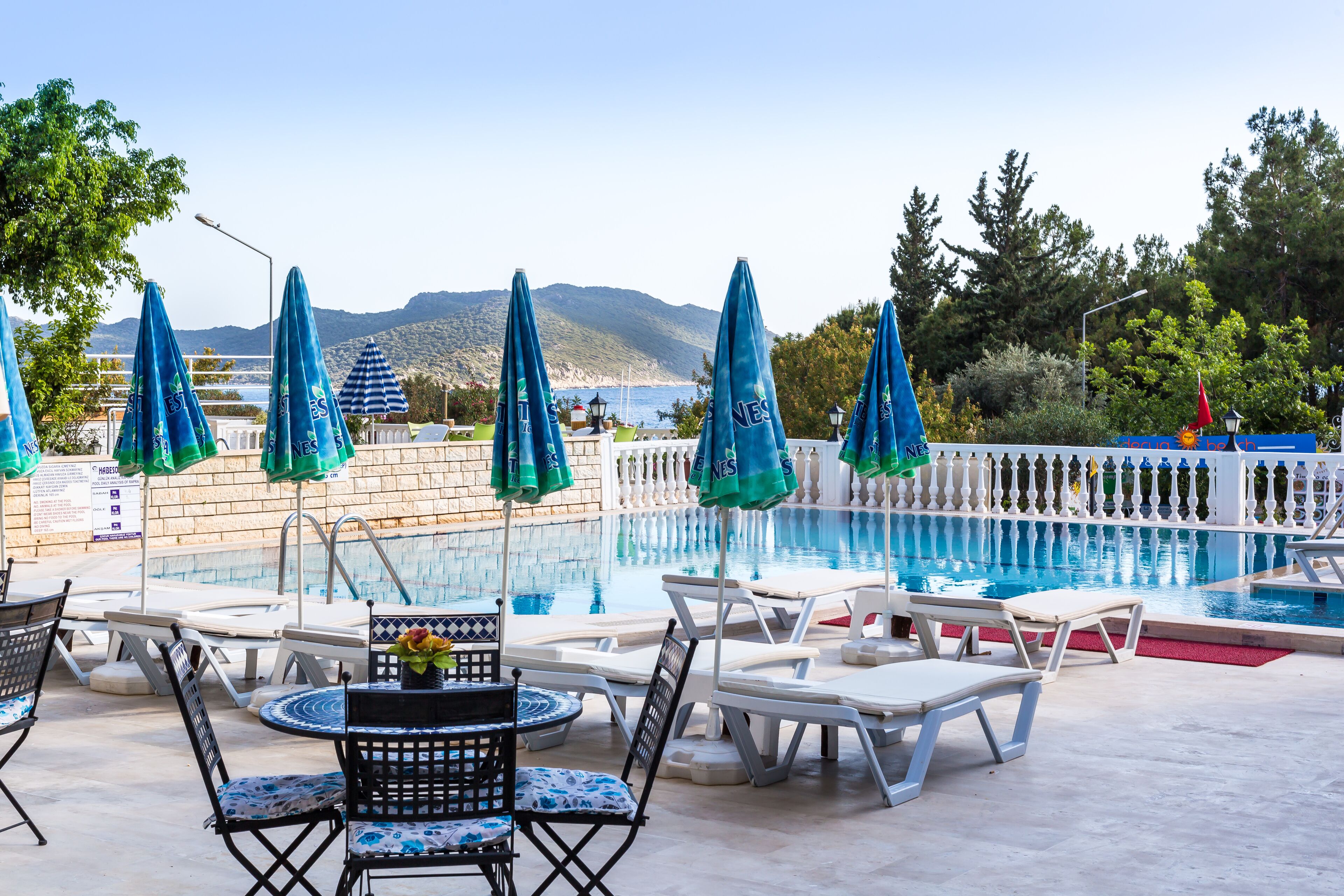 Zona de piscina con sillones de descanso, sombrillas y vistas al mar y a las montañas.