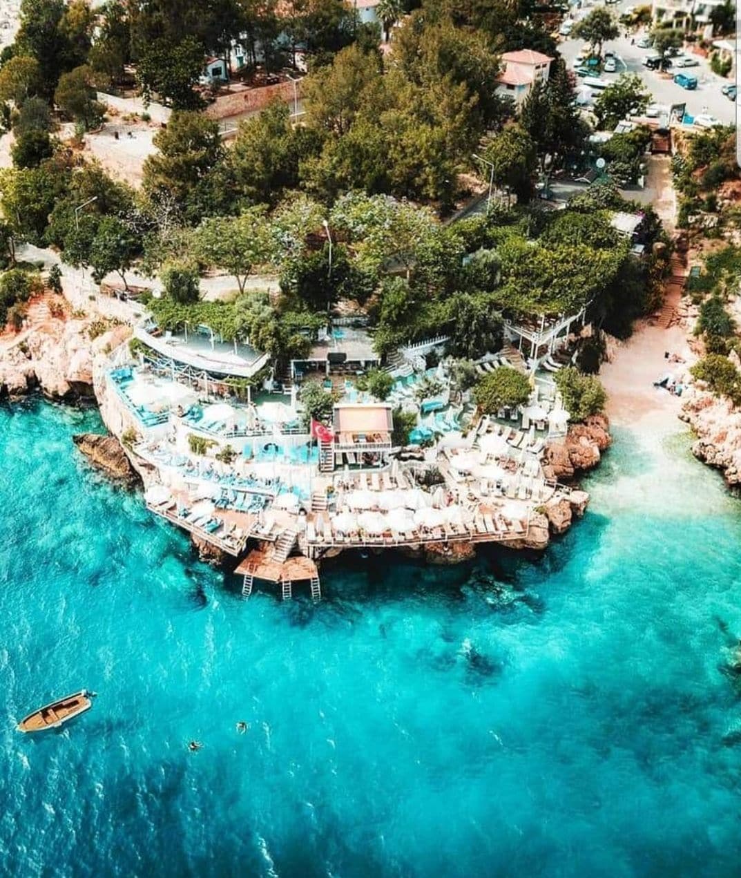 Una vista aerea di un resort con area piscina circondata da roccia e alberi, collegato alla terraferma da un ponte.