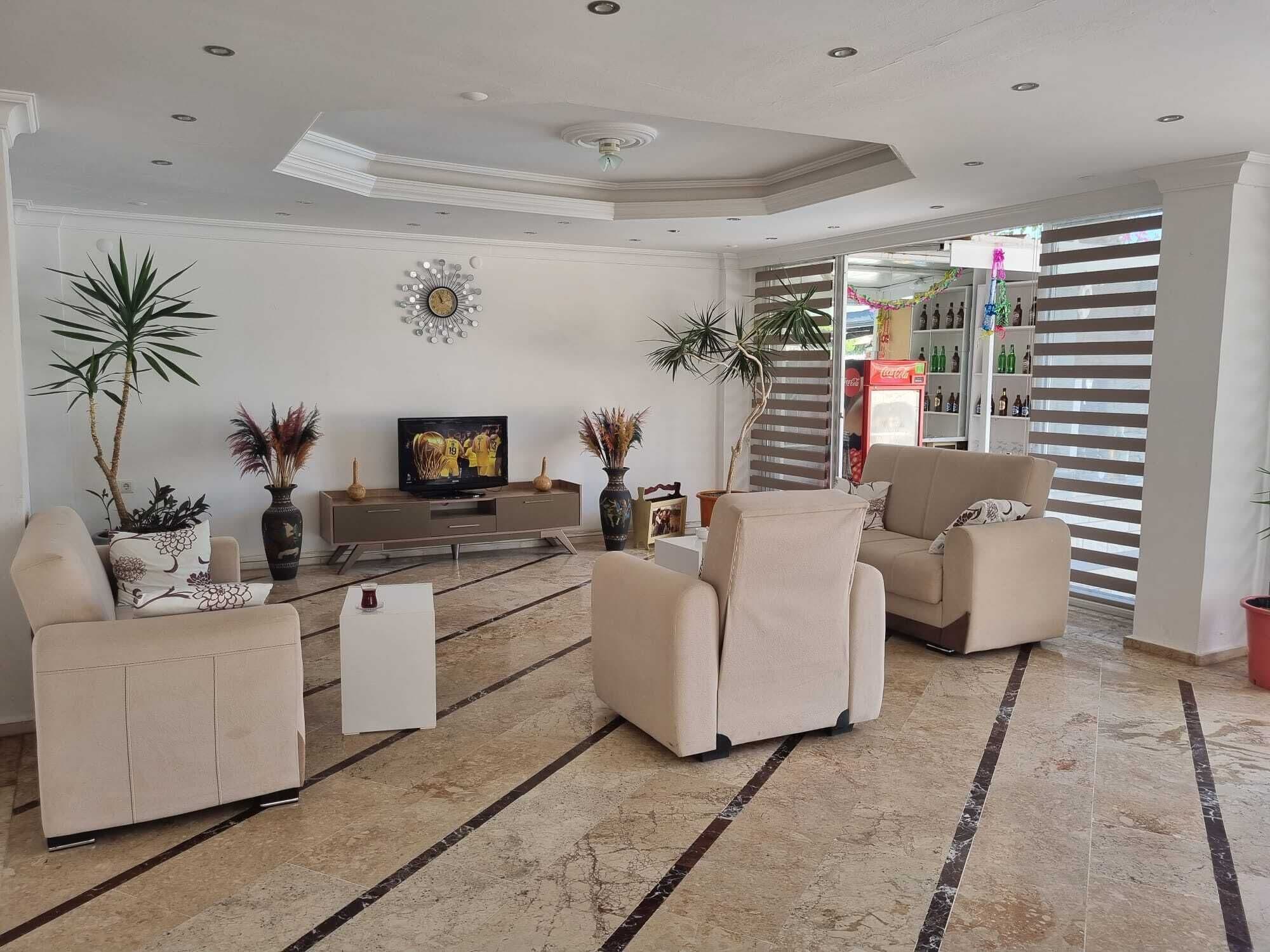 Uma sala de estar ampla com televisão moderna, assentos confortáveis e plantas decorativas.