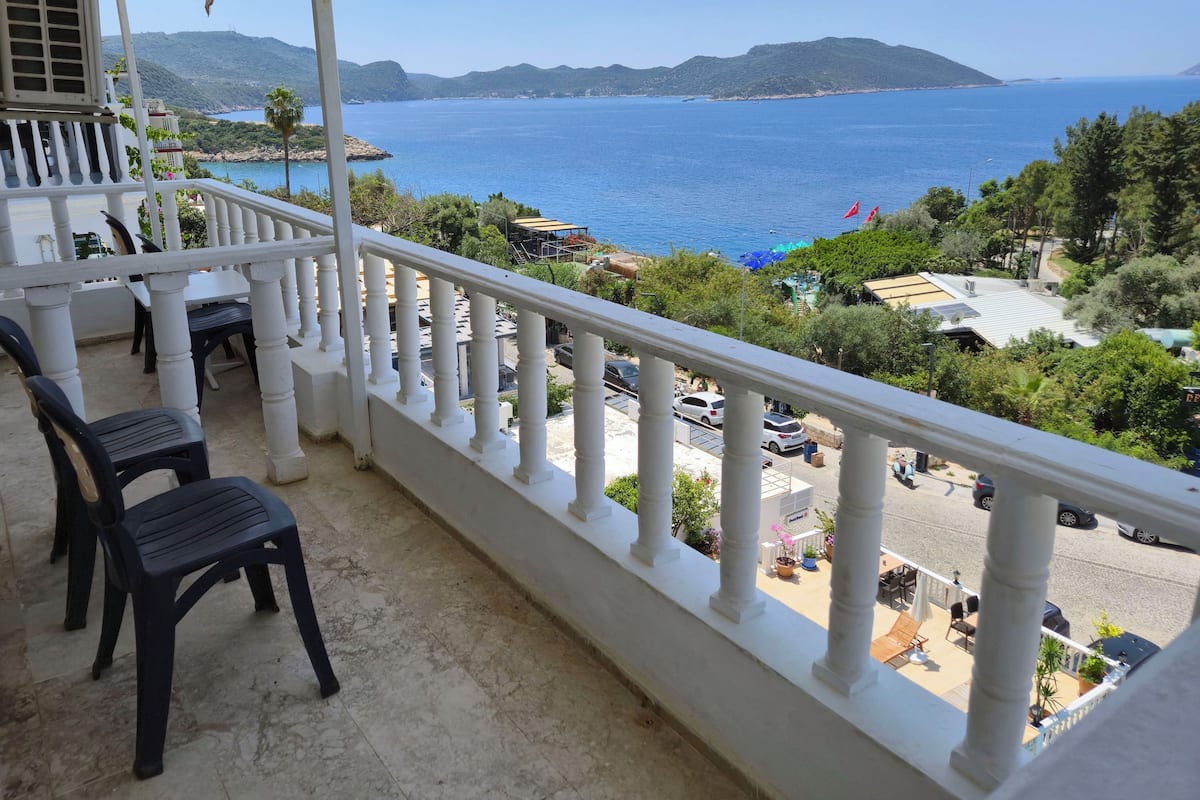 Varanda com vista para o mar e montanhas, com mesa e cadeiras.