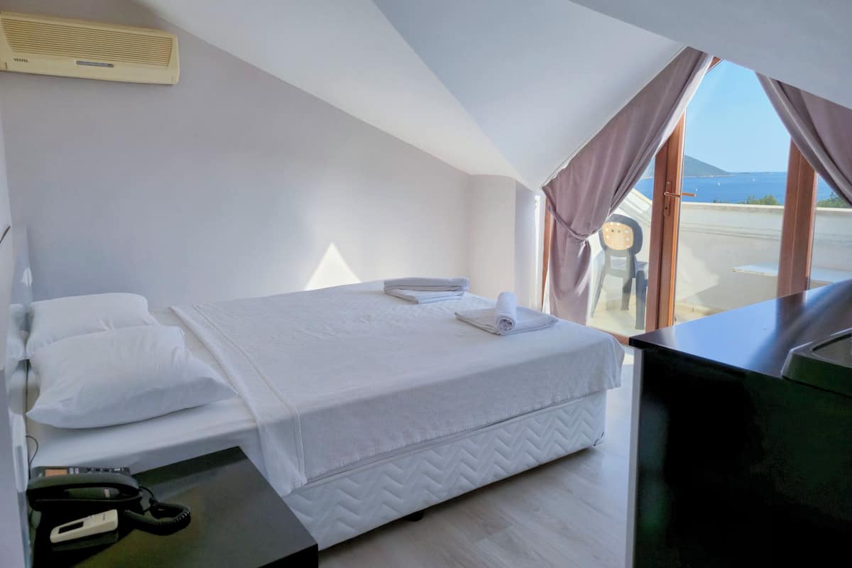 Quarto de hotel com cama, escrivaninha, cadeira e vista para o mar.