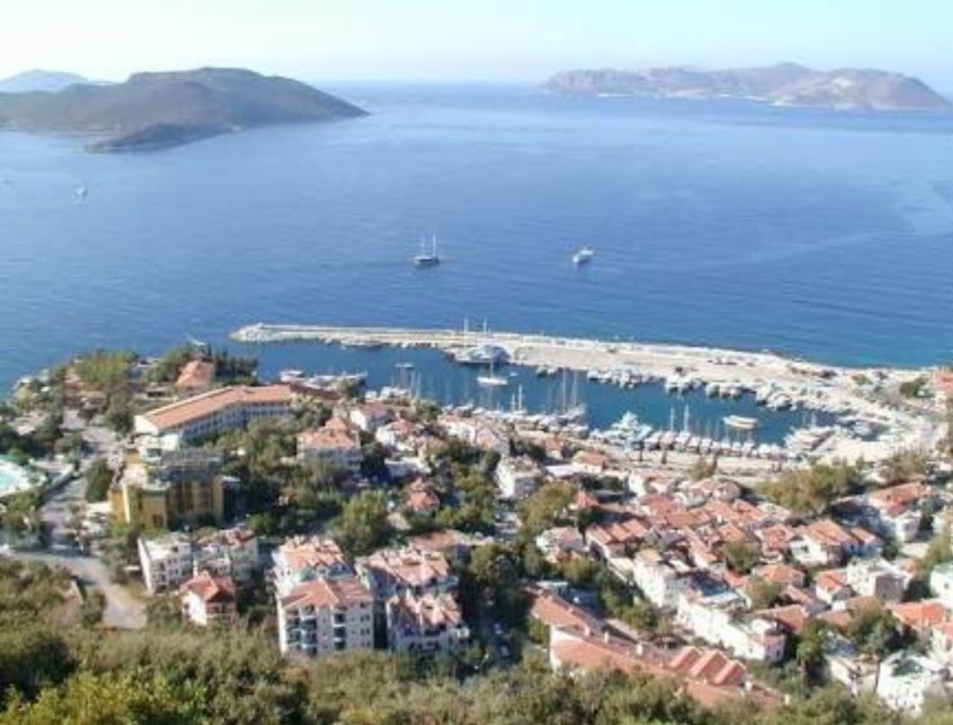 A coastal town with a marina, residential buildings, and a mountainous backdrop.