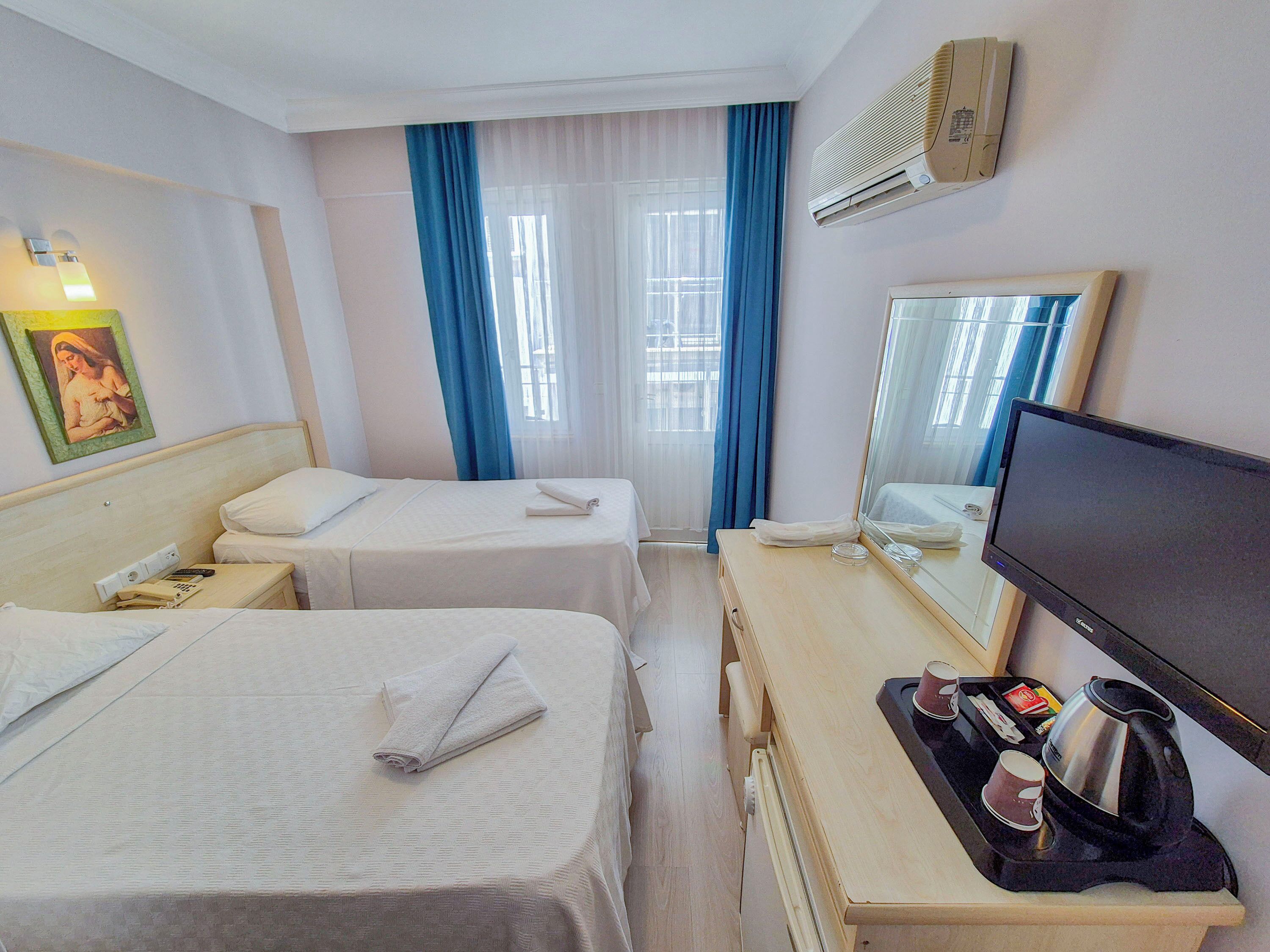Una habitación de hotel con dos camas, un escritorio con cafetera, un televisor y una ventana con cortinas.