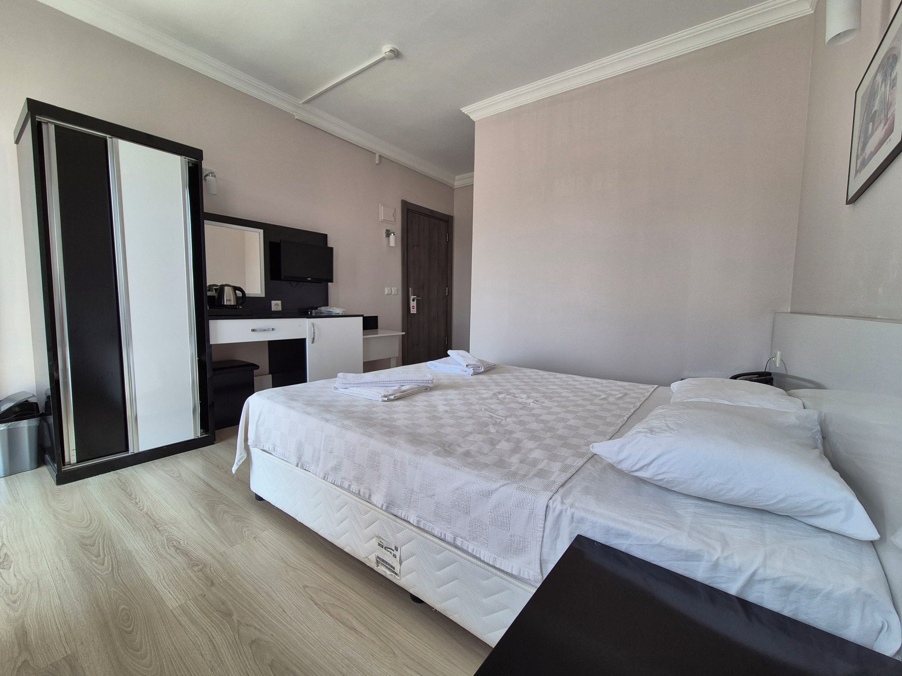 A hotel room with a large bed, a desk with a chair, a mirror, and a wardrobe.