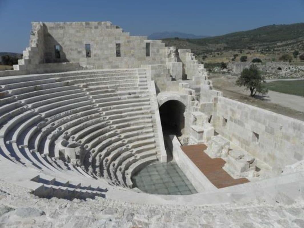 An ancient amphitheater with tiered seating and a central stage area.