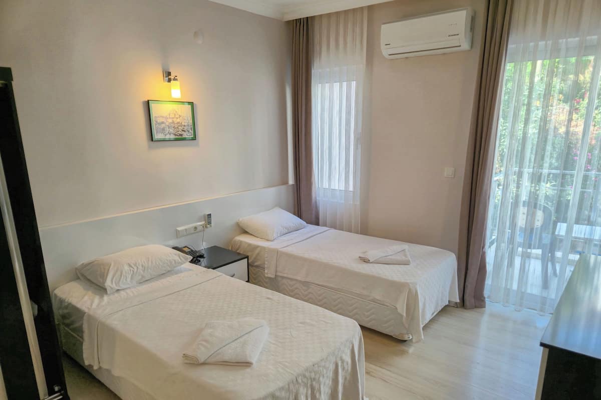 Quarto de hotel com duas camas, uma mesa de cabeceira com telefone, unidade de ar condicionado e janela com cortinas.