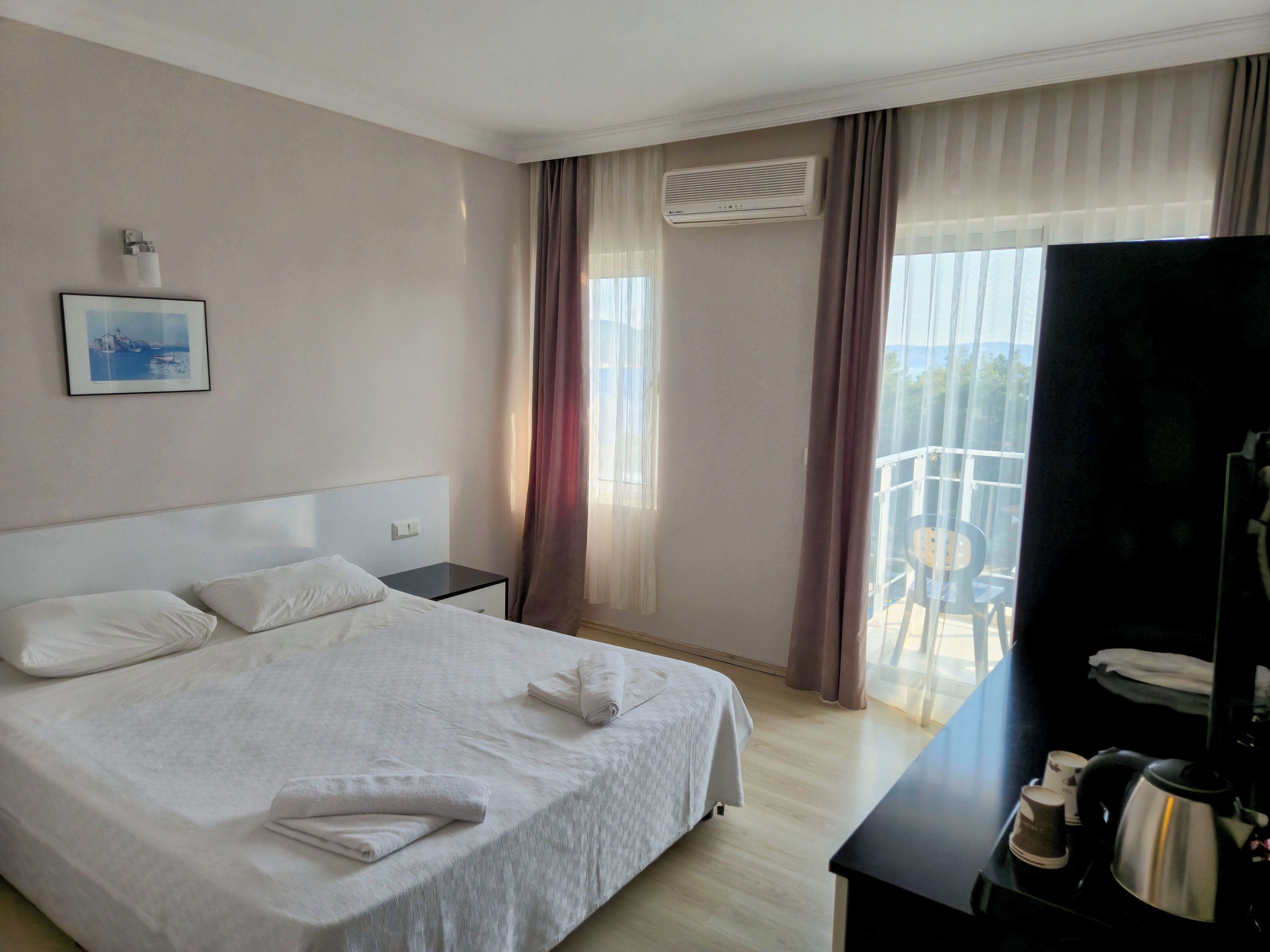Hotellihuone, jossa on sänky, yöpöytä, työpöytä, kahvinkeitin ja televisio.
