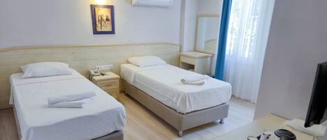 A hotel room with two beds, a bedside table with a phone and a lamp, a desk with a mirror, and a window with curtains.
