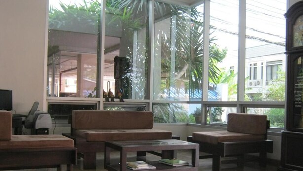 A room with large windows, a sofa, a coffee table, and a clock. - Tongtip Place (Bangkok)