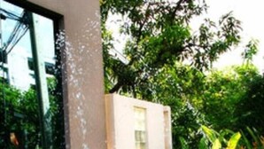 A rectangular water feature with two streams of water, surrounded by greenery and a building with a glass facade. - Tongtip Place (Bangkok)