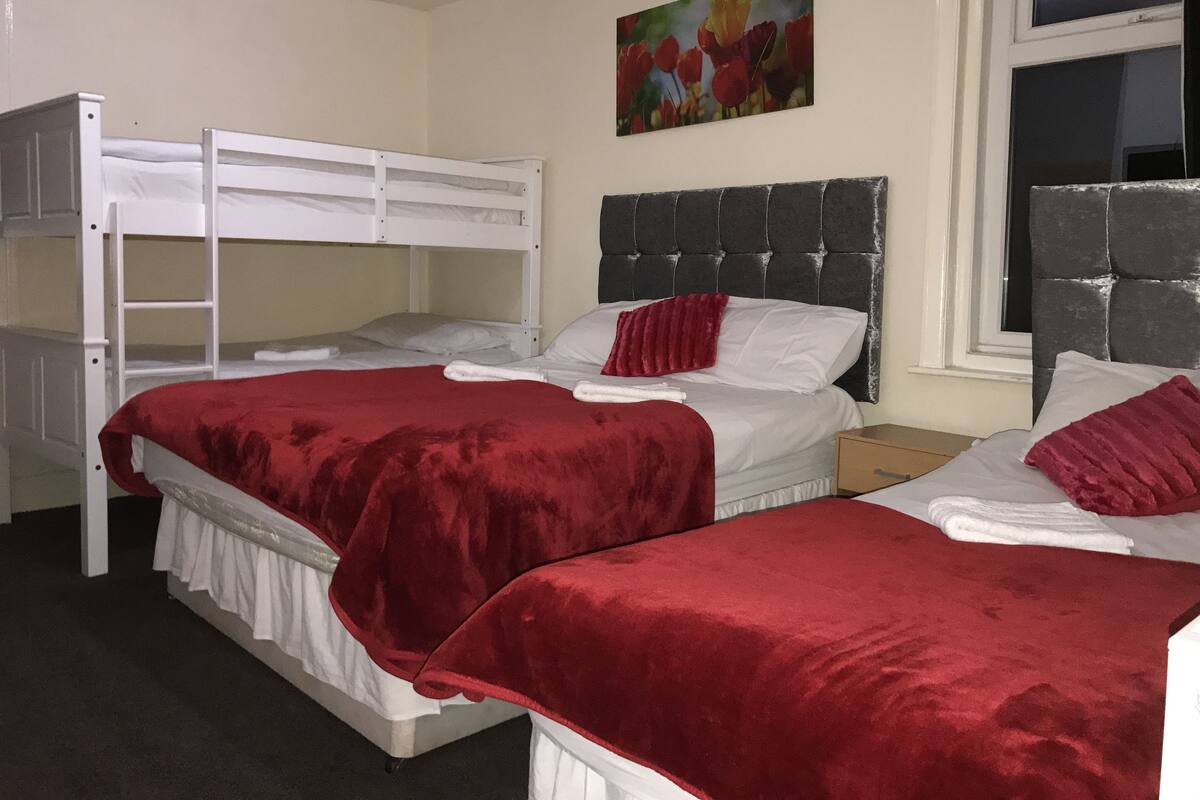 A dormitory room with bunk beds, a red blanket, and a painting of flowers on the wall.