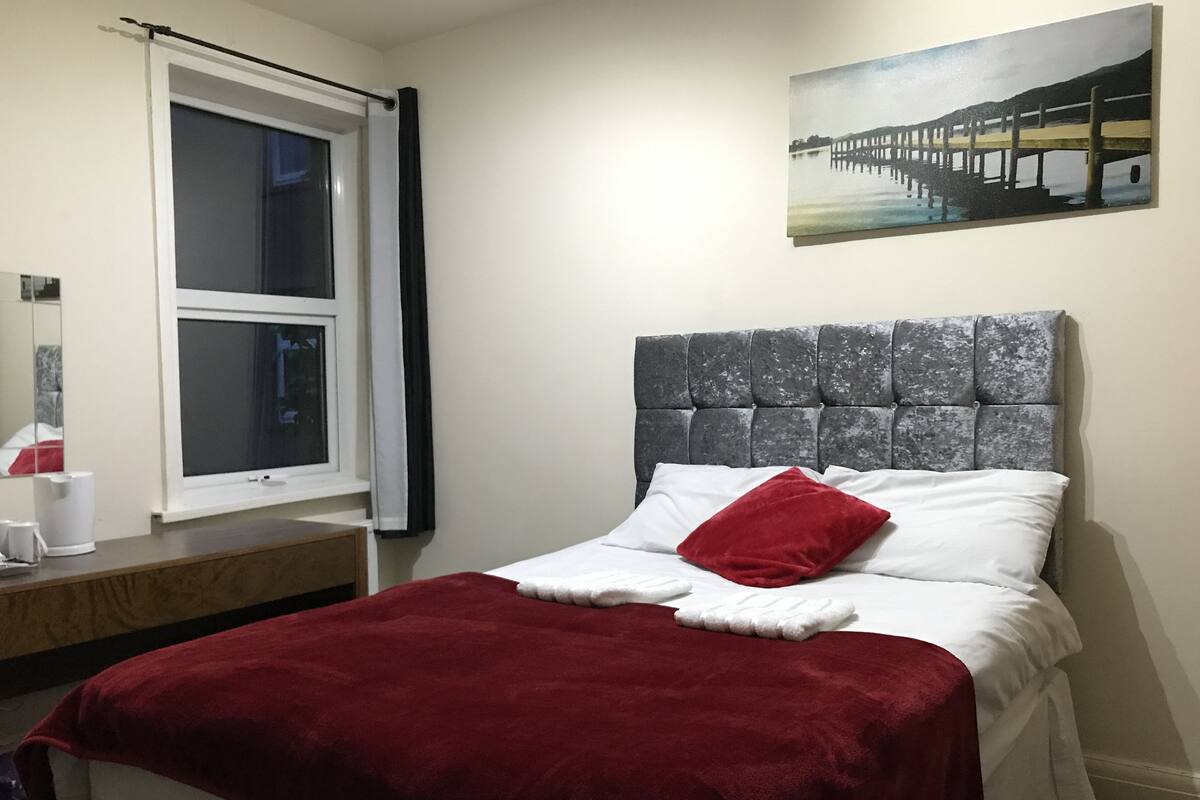 A bedroom with a bed, a window, a painting, and a bedside table.