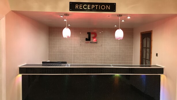 A reception area with a black counter, a sign reading "RECEPTION," and a wall with a geometric pattern and a logo. - Hello Roomz (Blackpool)