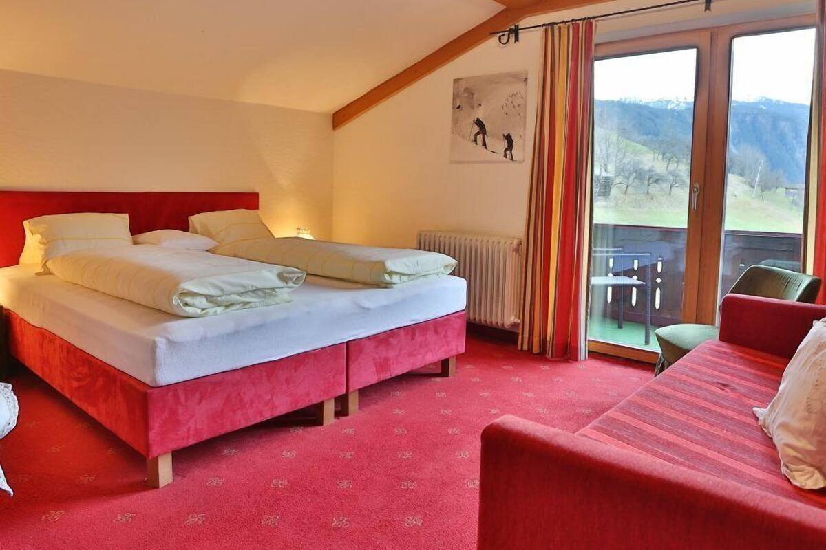 A hotel room with a large bed, a red sofa, a view of the outdoors, and a painting on the wall.