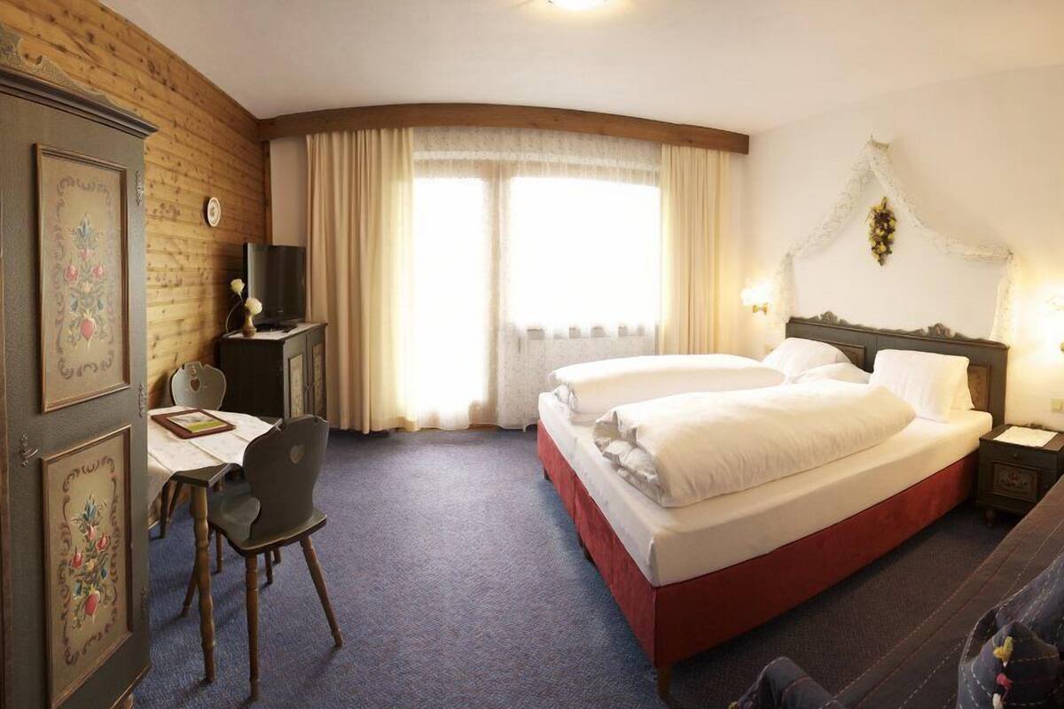 A hotel room with a large bed, a desk with a chair, a television, and a window with curtains.