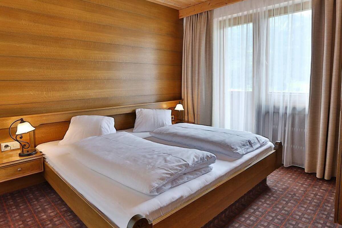 A double bed with white linens in a room with wooden paneling and a patterned carpet.