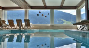 A pool area with lounge chairs and large windows overlooking a mountainous landscape. - Hotel Fliesserhof (Fliess)