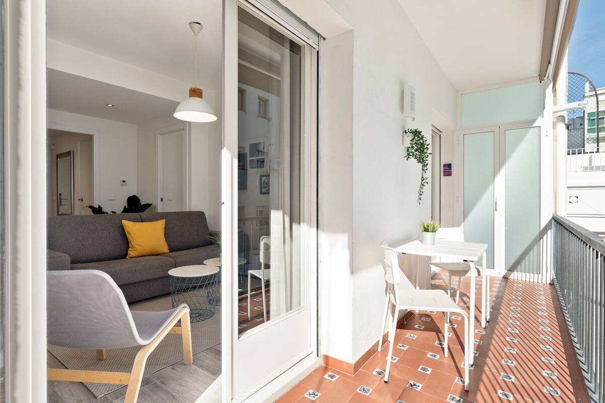 A balcony with a seating area, a small table, and a sofa with a yellow pillow.