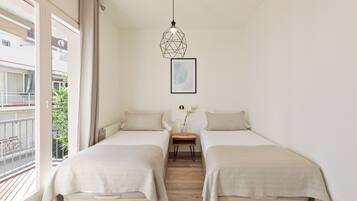 A bedroom with two beds, a wooden floor, a window with a view of a balcony, and a hanging light fixture.