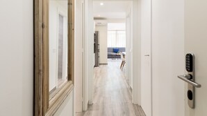 Un couloir avec, au fond, une cuisine moderne, un coin repas avec une table et des chaises, et une porte dotée d’un système de verrouillage à clavier.