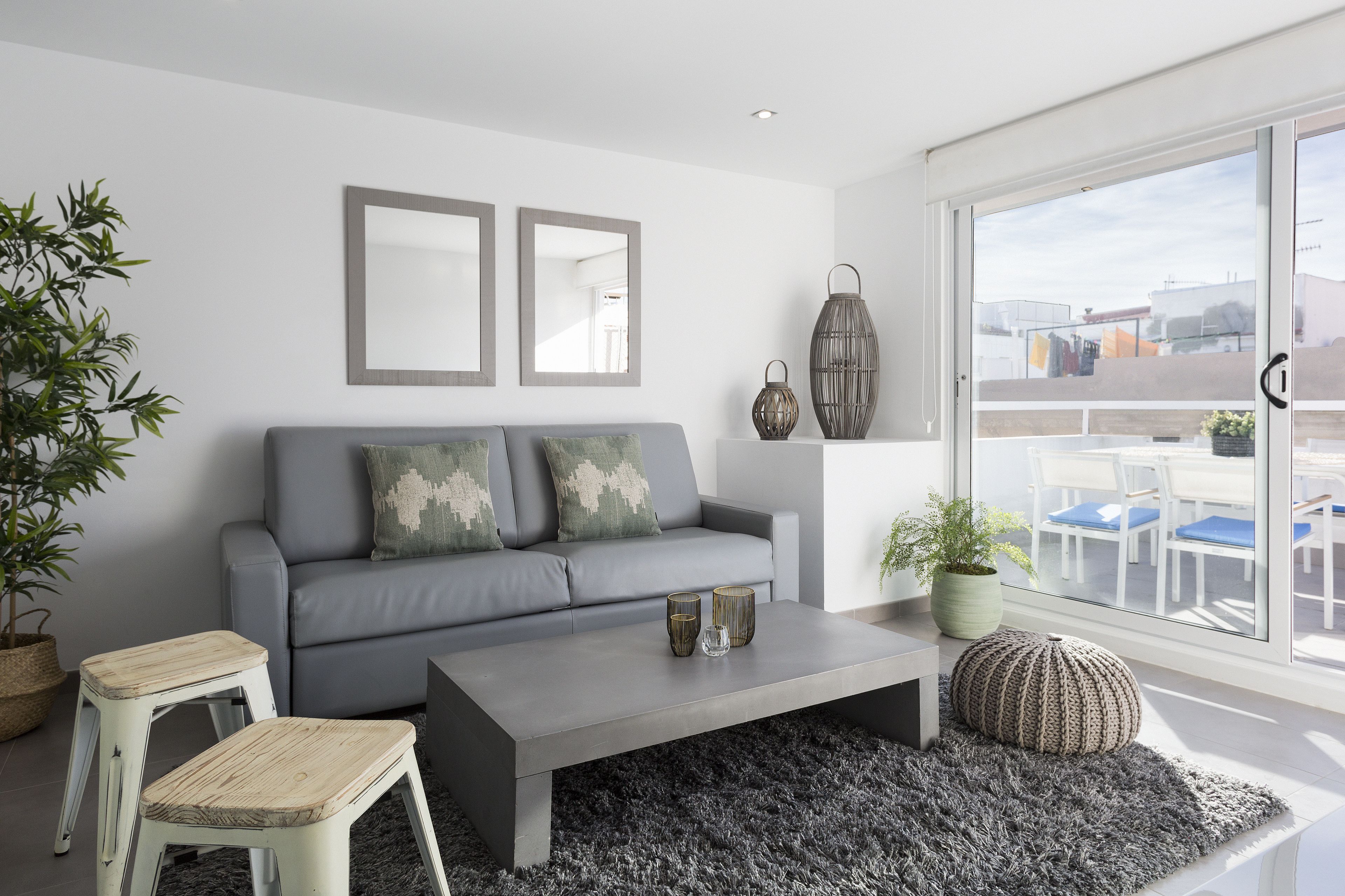 Una sala moderna con un sofá gris, dos espejos enmarcados, una mesa de centro y un ventanal con vistas al exterior.